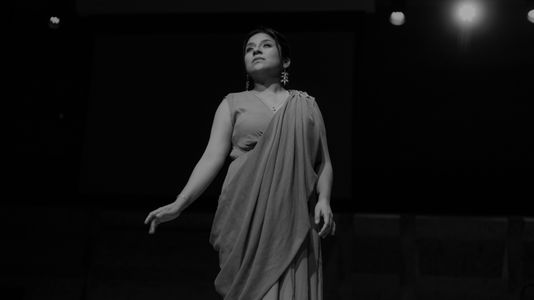 Mariela in a draped outfit stands confidently under stage lights