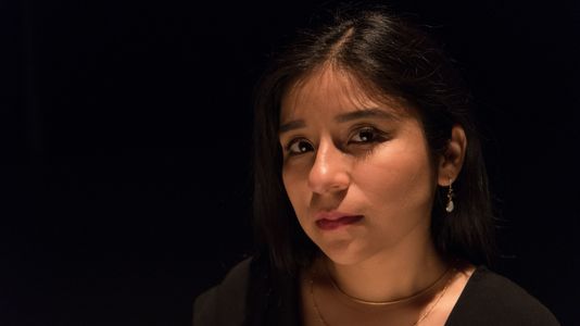 Mariela gazes gently at the camera against a dark background